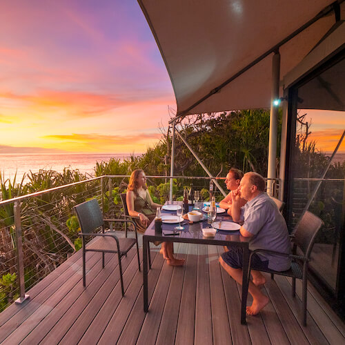 Couple enjoying a gourmet sunset dinner on their ecolodge deck with luxury accommodation provider Swell Lodge.